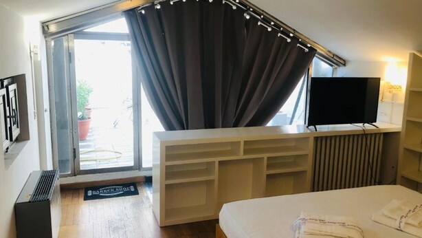 A hotel room with a bed, a TV, a sliding glass door, and a built-in bench with storage. - LA TERRAZZA DI AIDA (Verona)