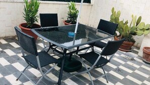 A glass-top table with four chairs, surrounded by potted plants, on a checkered floor. - LA TERRAZZA DI AIDA (Verona)