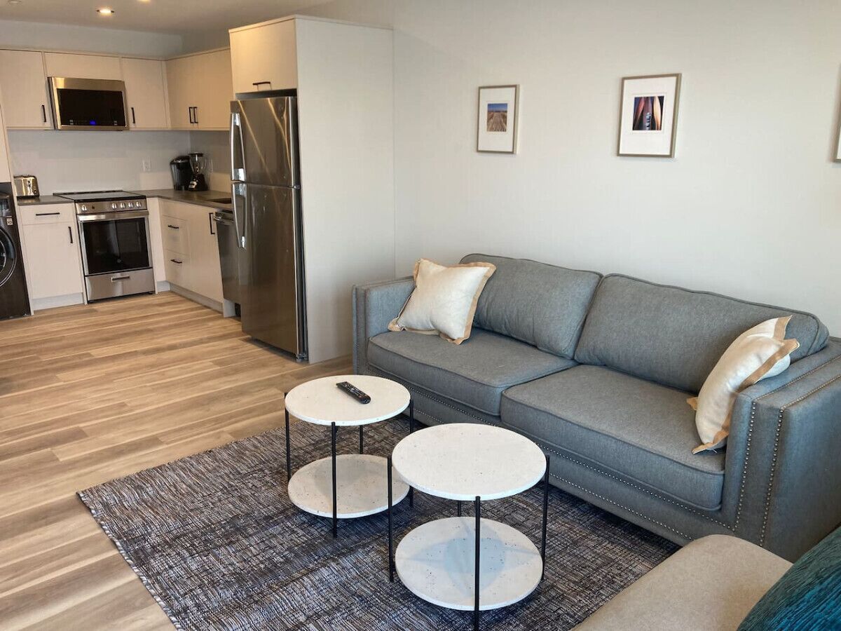 A modern kitchen with stainless steel appliances, a grey sofa, and two small tables.