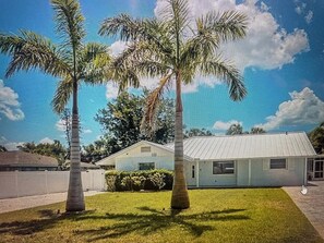 Standalone house with a flat roof, surrounded by a well-maintained lawn and palm trees.