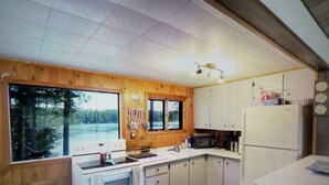 A compact kitchen with wooden cabinets, a microwave, and a sink. - Charming 2-bedroom cottage lake property with kayaks firepit and Great fishing! (Elcho)