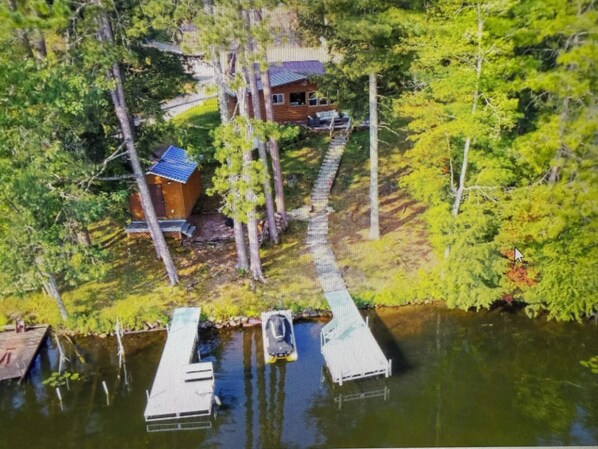 A house with a dock extending into a body of water, surrounded by dense greenery.