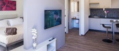 A modern hotel room with a bed, a TV, a small kitchen area, and a dining space.