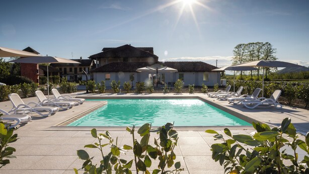 Una piscina con lettini e ombrelloni, circondata da edifici e vegetazione.