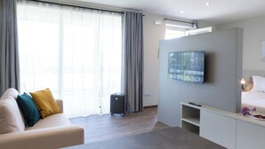 Una moderna camera d'albergo con divano, televisione a parete, un letto e un'ampia finestra con tende.