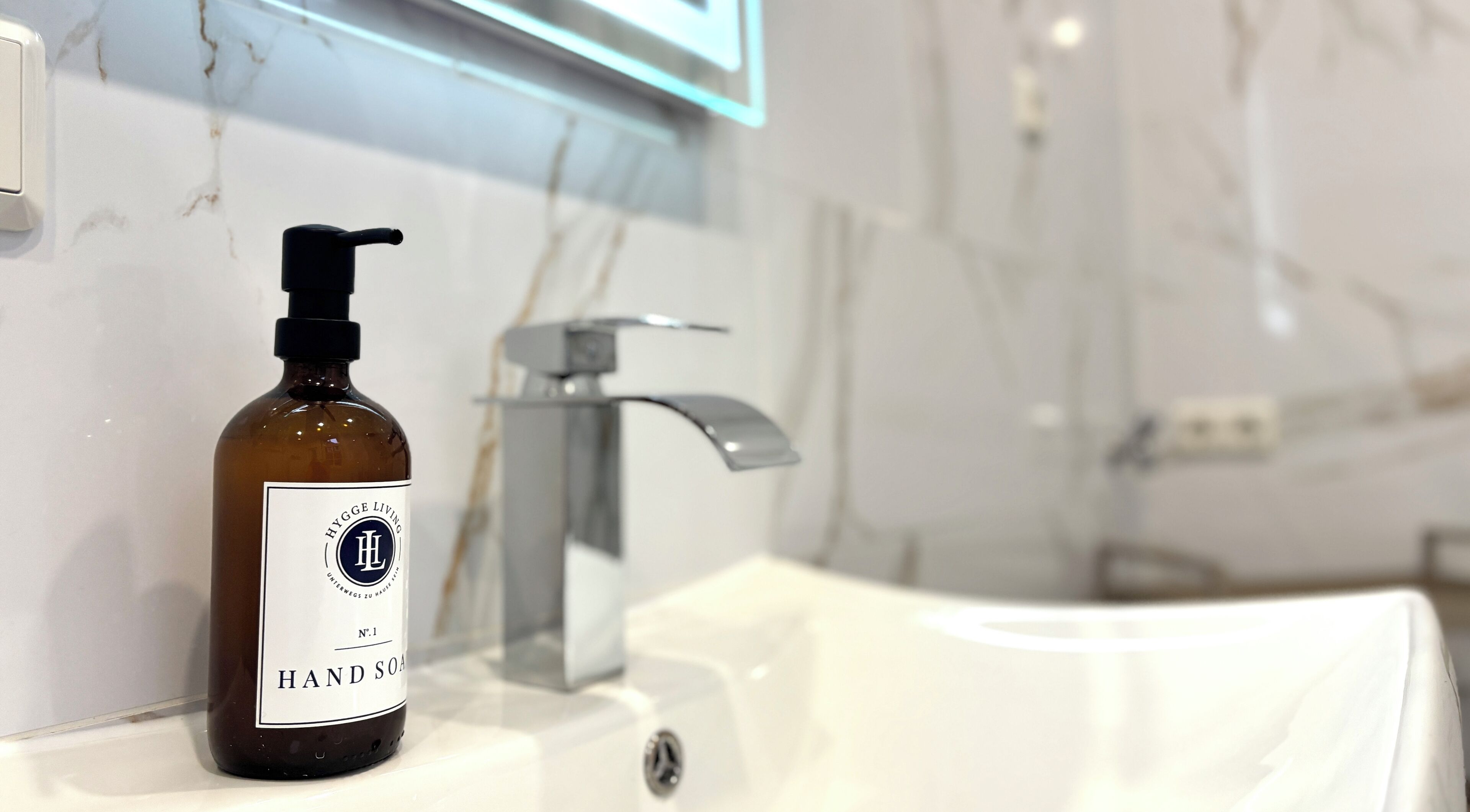A bathroom with a white marble sink, a modern faucet, and a bottle of hand soap labeled 'HYGGE LIVING'.