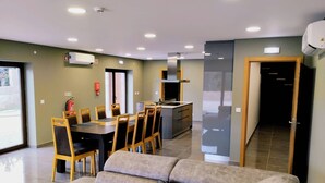 A modern living room with a sofa, dining table, and chairs. There is a kitchen area with a stove and cabinets.