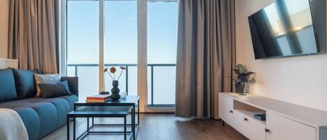 A modern living room with a sofa, a coffee table, a TV, and a balcony with curtains.