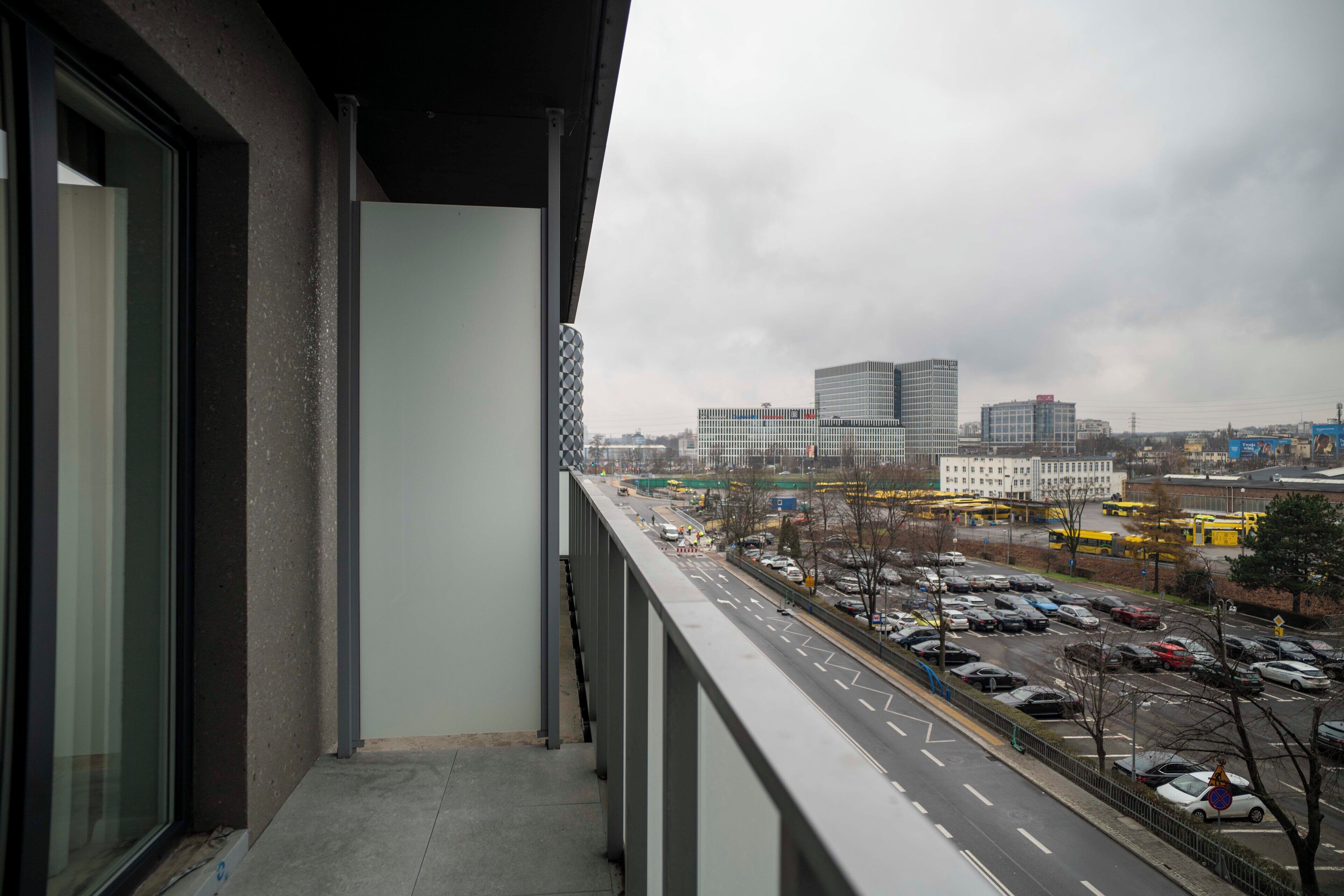 A balcony with a view of a cityscape, including buildings and a busy road with cars and buses.