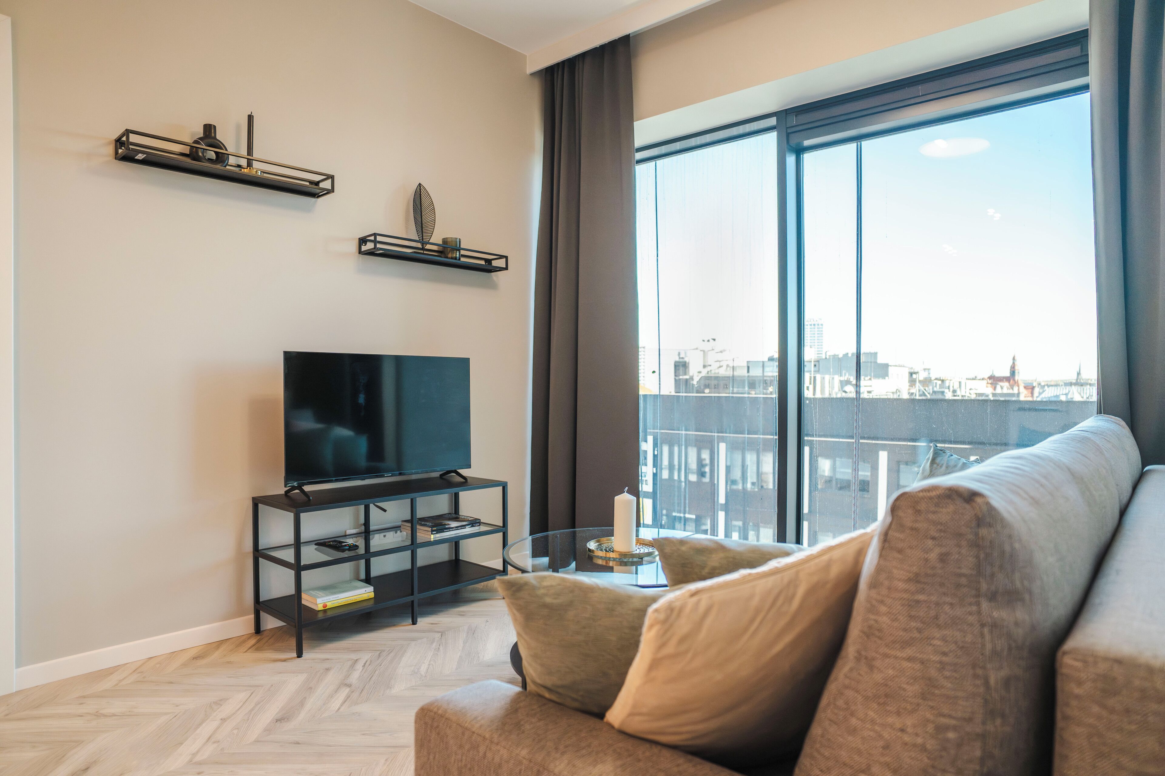 A modern living room with a large window, a flat-screen TV, and a sofa.