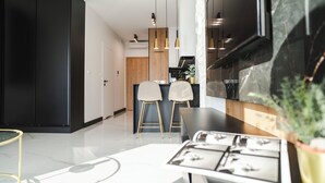 A modern kitchen with a black cabinet, two bar stools, pendant lights, and a marble countertop. - Global Apartments (Katowice)