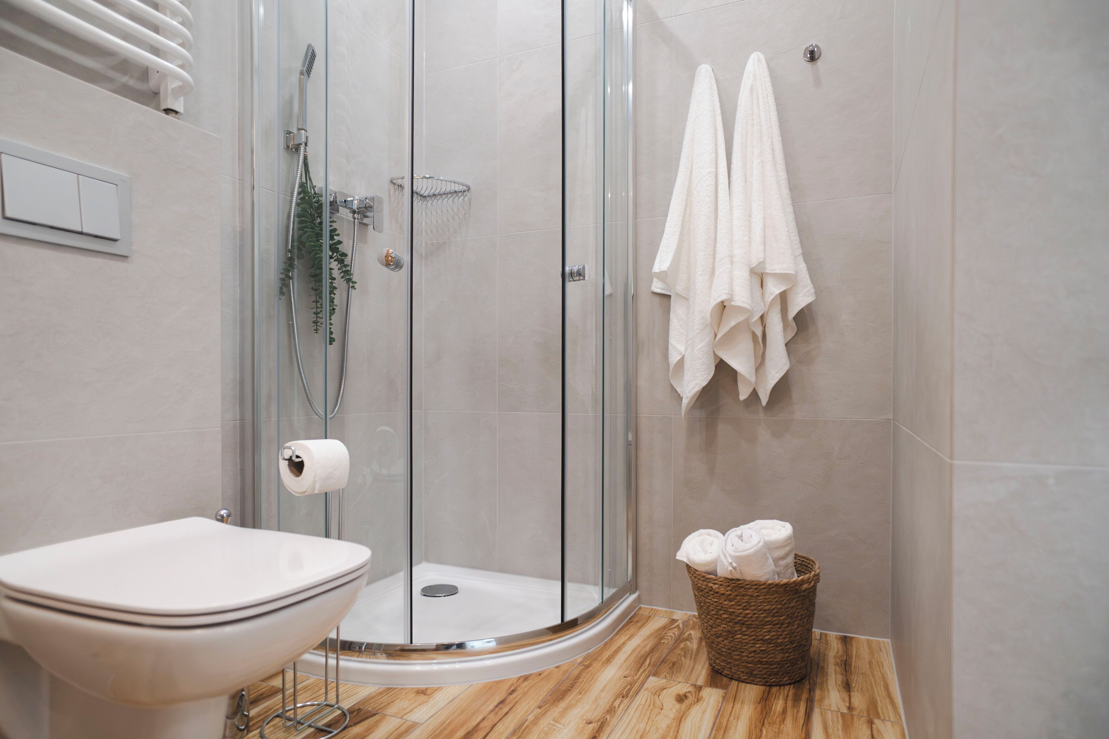 A modern bathroom with a glass-enclosed shower, a toilet, and a basket of towels.