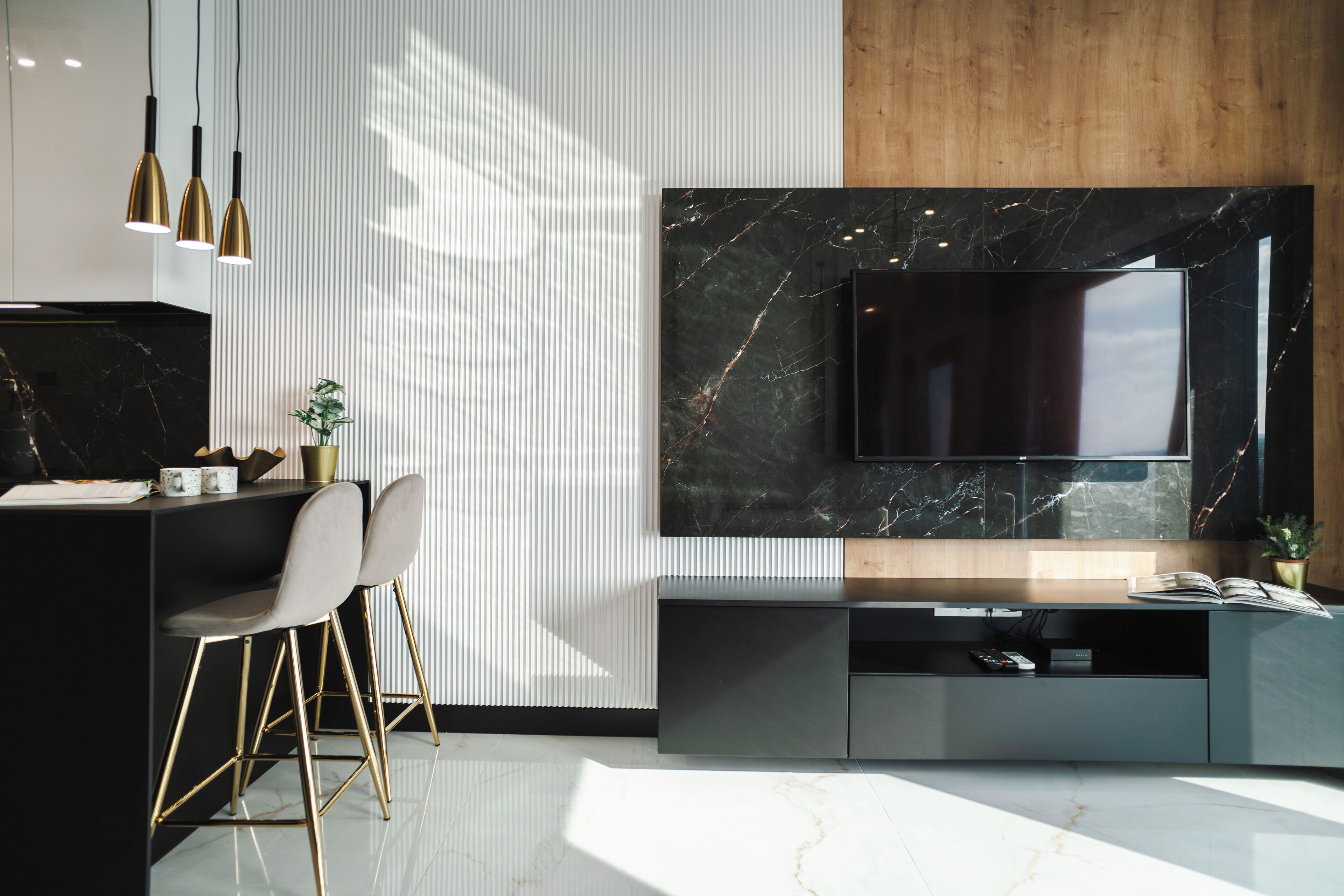 A modern kitchen with a marble backsplash, a built-in TV, and a dining area with bar stools.