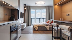 A modern hotel room with a kitchenette, a large bed, a view of the city, and a balcony. - Global Apartments (Katowice)