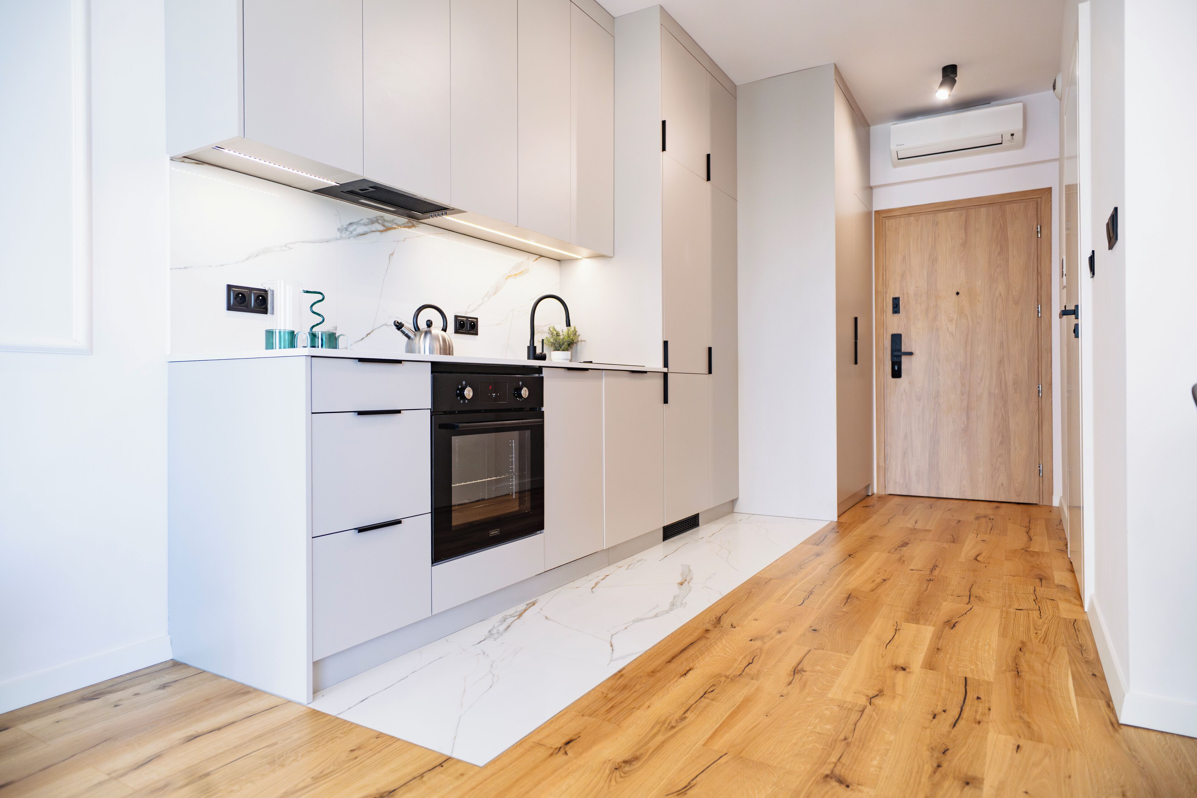Une cuisine moderne avec des meubles blancs, un four encastré et un plancher en bois.