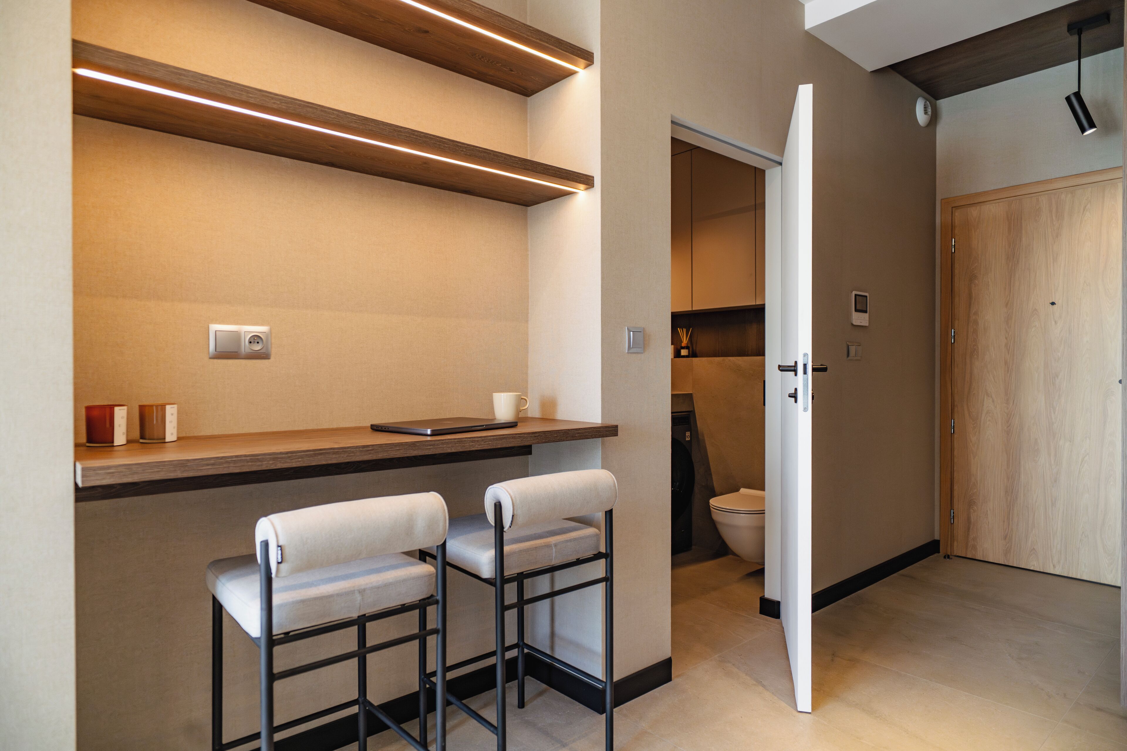 Une cuisine moderne avec un plan de travail en bois, deux tabourets de bar et une porte blanche donnant sur une salle de bain.