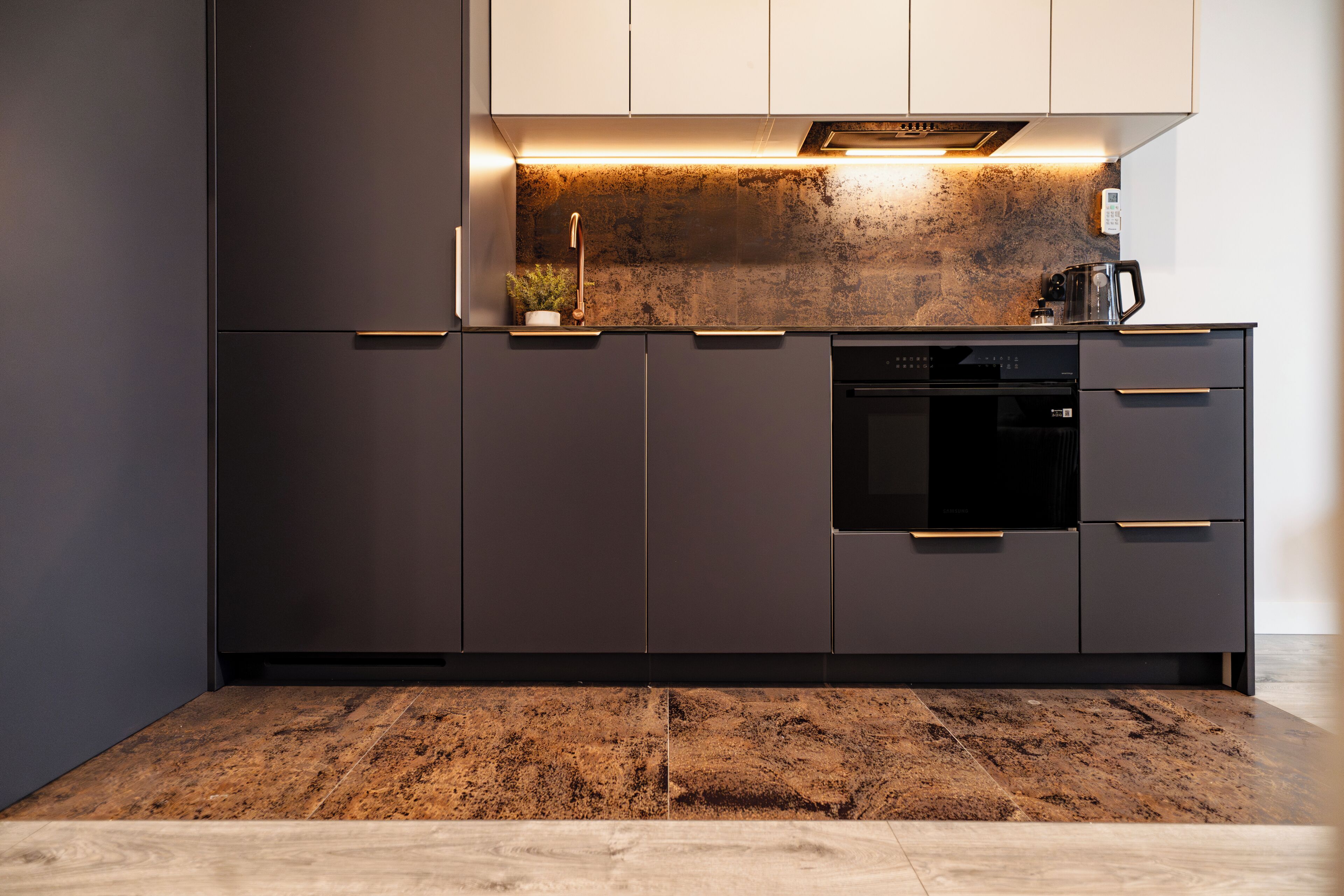 A modern kitchen with dark cabinetry, a stainless steel range hood, and a built-in oven.