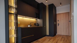 A modern kitchen with dark cabinetry, a built-in wine rack, and a wooden floor. - Global Apartments (Katowice)