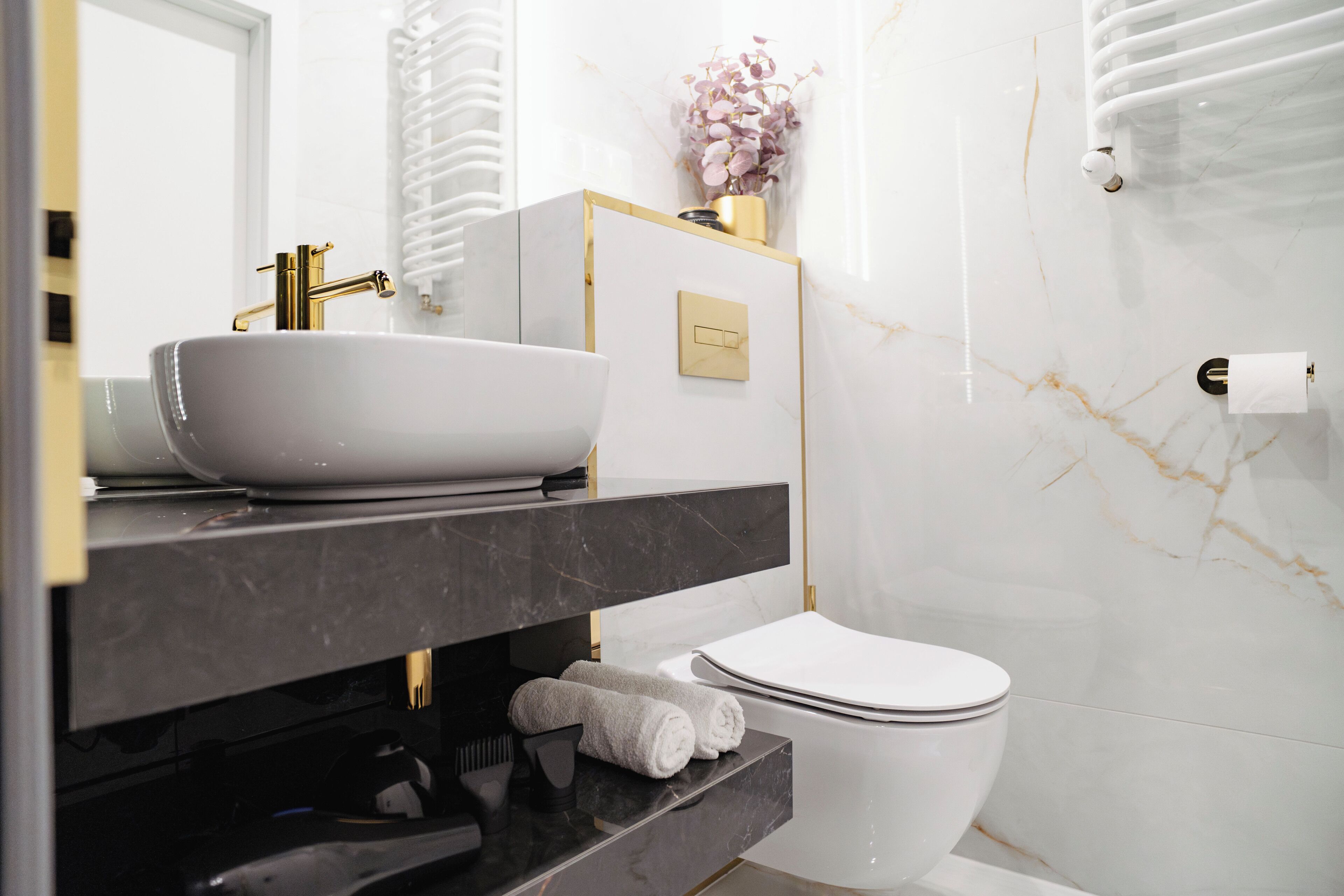 Ein modernes Badezimmer mit Waschbecken in Weiß, Wasserhahn in Gold und Marmorwänden.