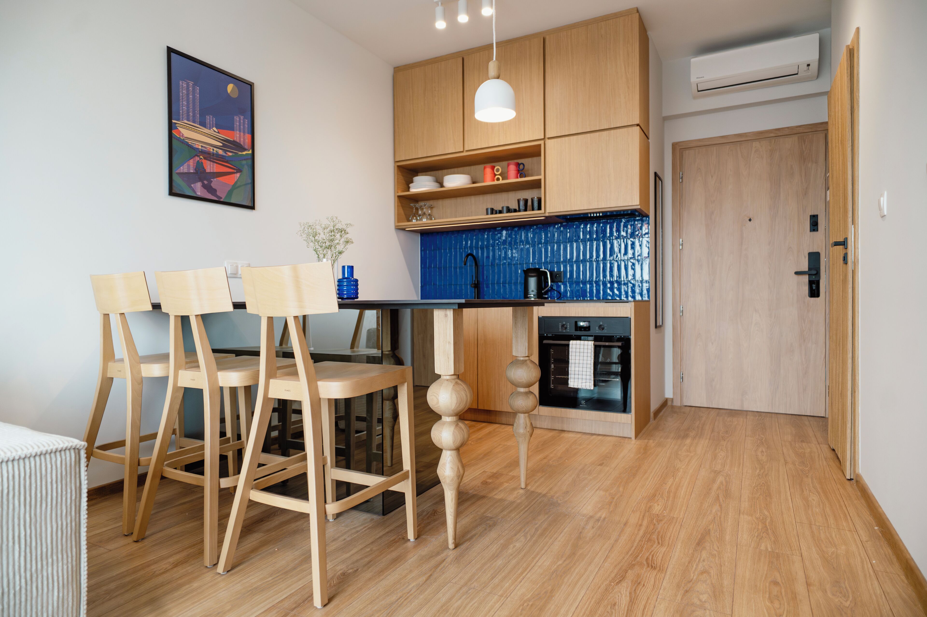 A modern kitchen with wooden cabinets, a blue backsplash, and a dining area with wooden chairs.