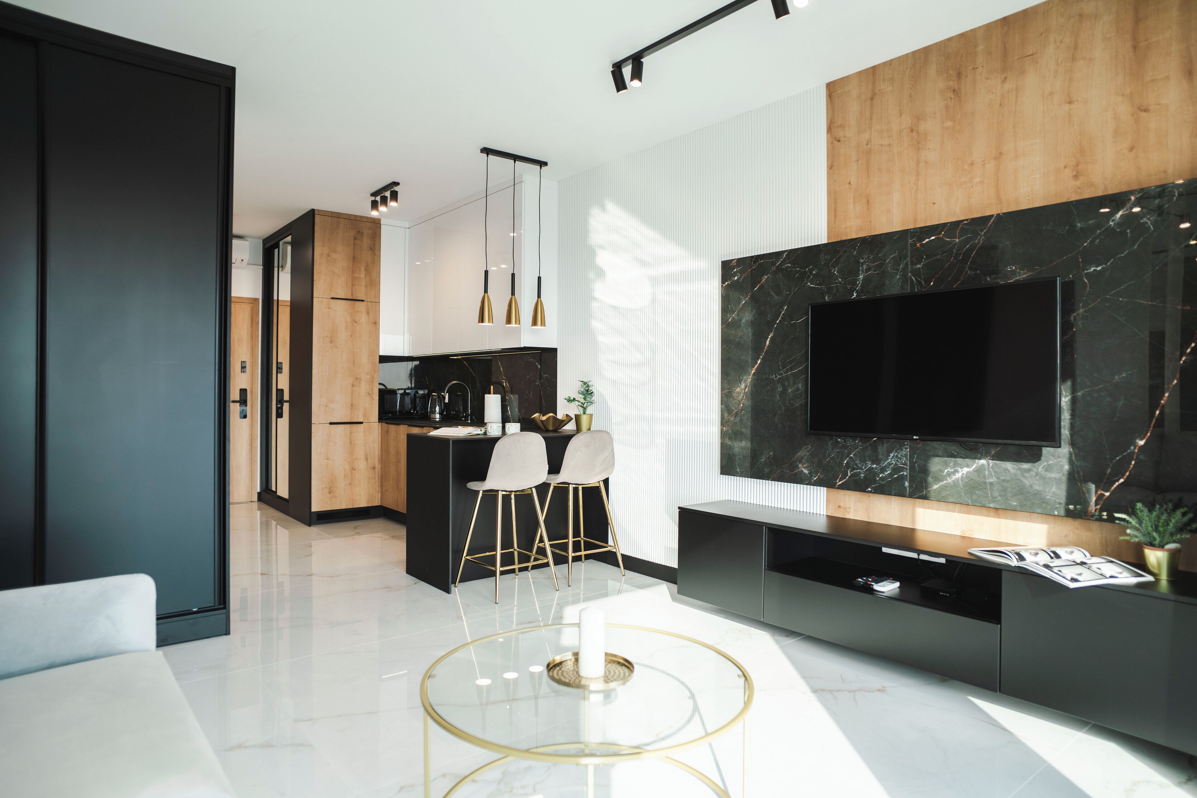 A modern kitchen with a central island, a dining area with two chairs, and a large TV mounted on a marble wall.
