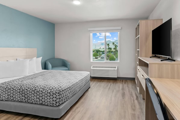 A modern hotel room with a bed, a TV, a desk, and a window with a view of the outdoors. - Woodspring Suites Tucson Medical Center (Tucson)