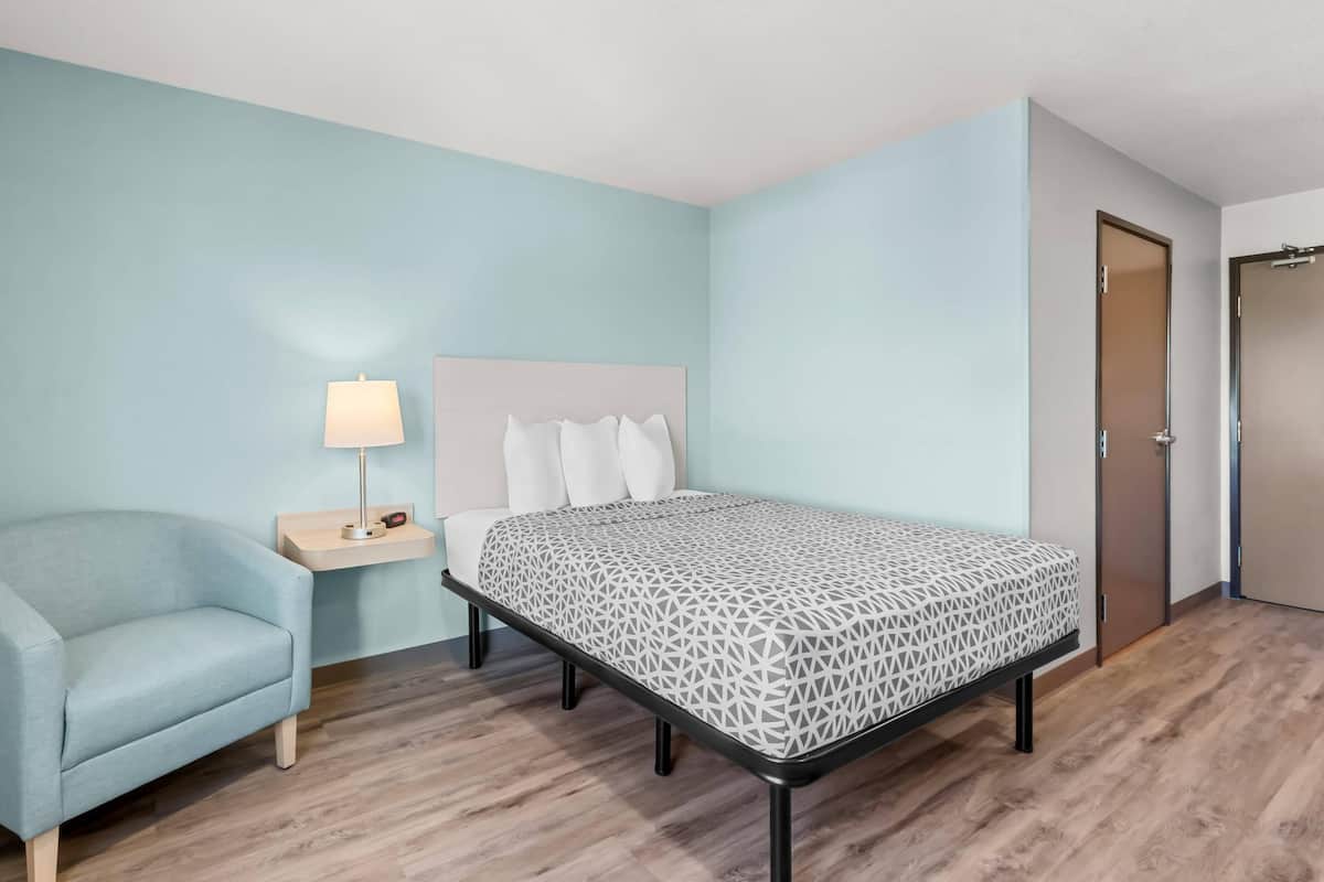 A bedroom with a bed, a nightstand, a lamp, and a chair.