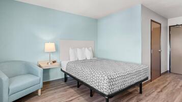 A bedroom with a bed, a nightstand, a lamp, and a chair.