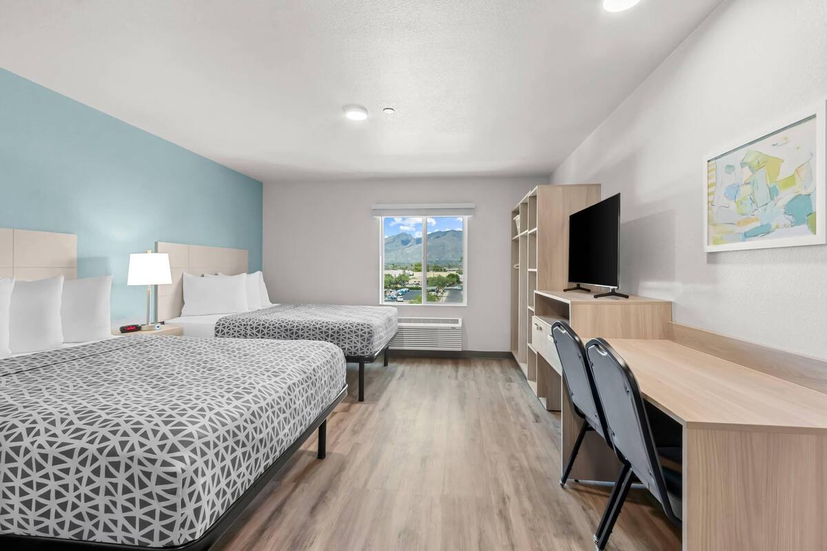 A hotel room with two beds, a desk, a TV, and a window with a mountain view.