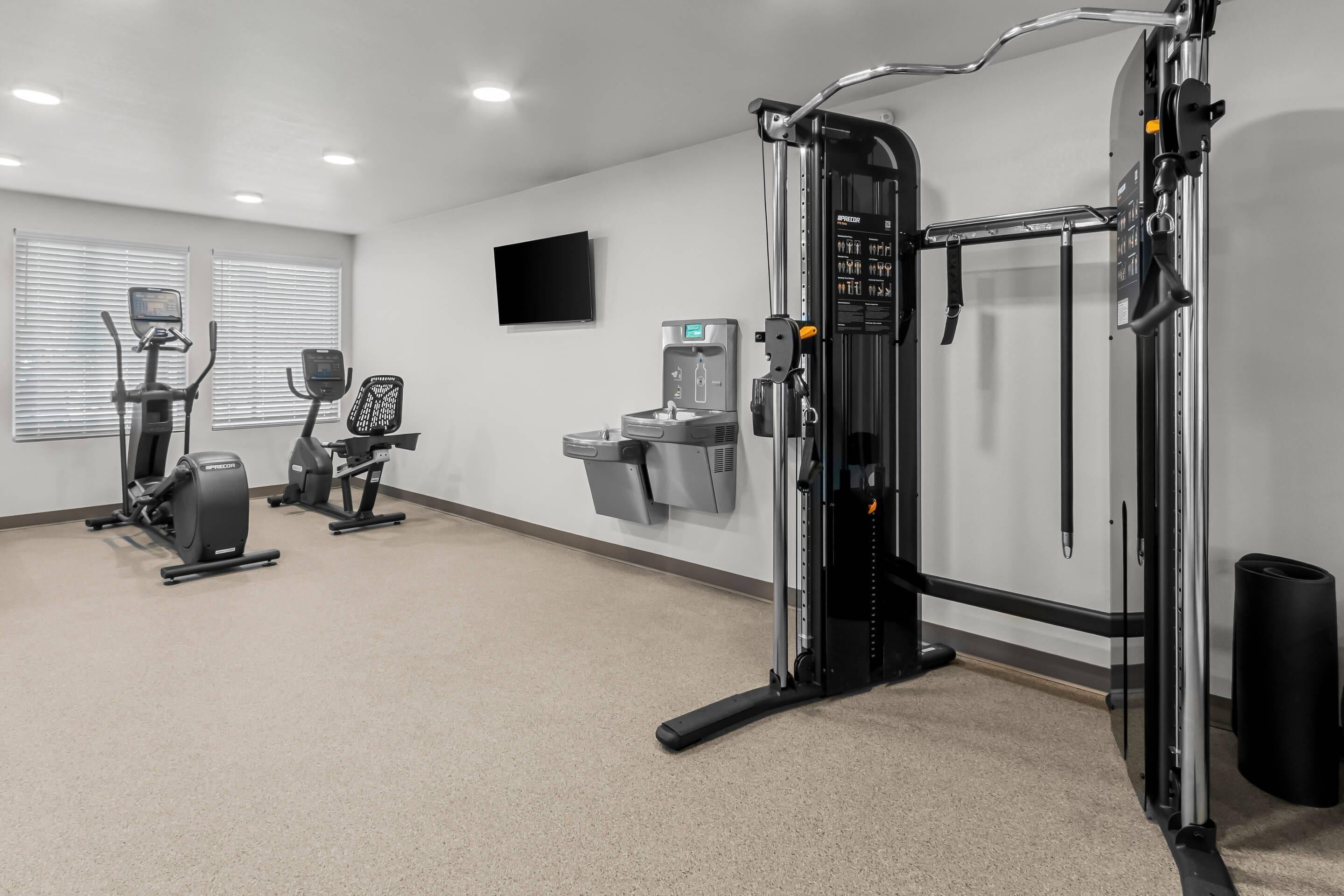 Academia com máquinas de cardio, um banco de musculação e um bebedouro.