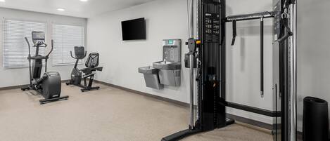 A gym with cardio machines, a weight bench, and a water dispenser.