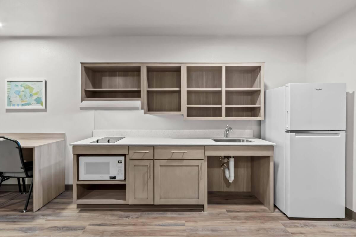 A modern kitchen with wooden cabinets, a built-in microwave, a sink, and a white refrigerator.
