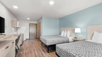 A hotel room with two beds, a desk with a chair, a TV, a lamp, and a door leading to the bathroom.