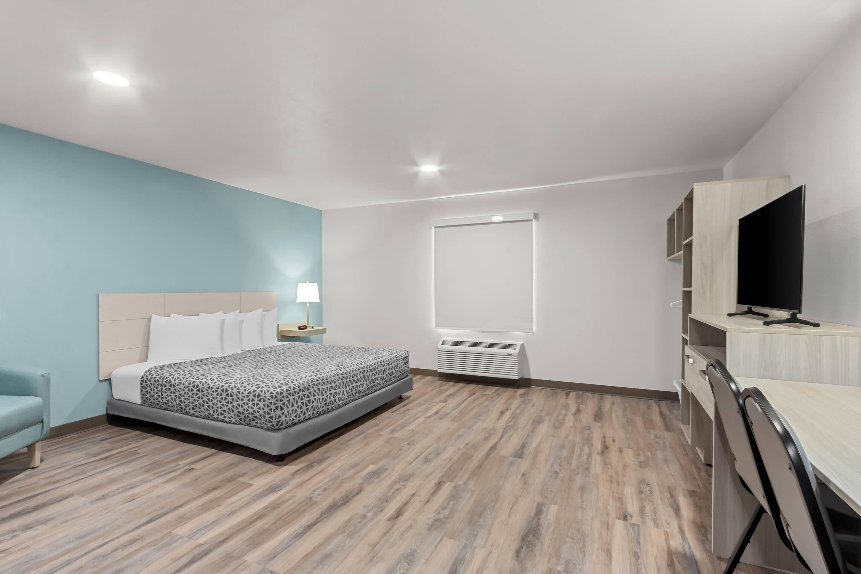 A modern hotel room with a bed, a desk, a TV, and a window.