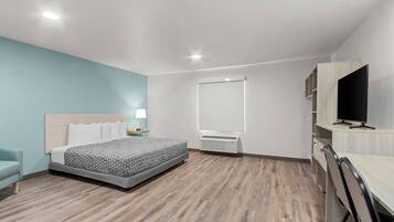 A modern hotel room with a bed, a desk, a TV, and a window.