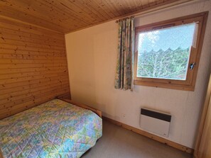 Ein kleines Zimmer mit einem Einzelbett, Holzwänden und einem Fenster mit Vorhängen.