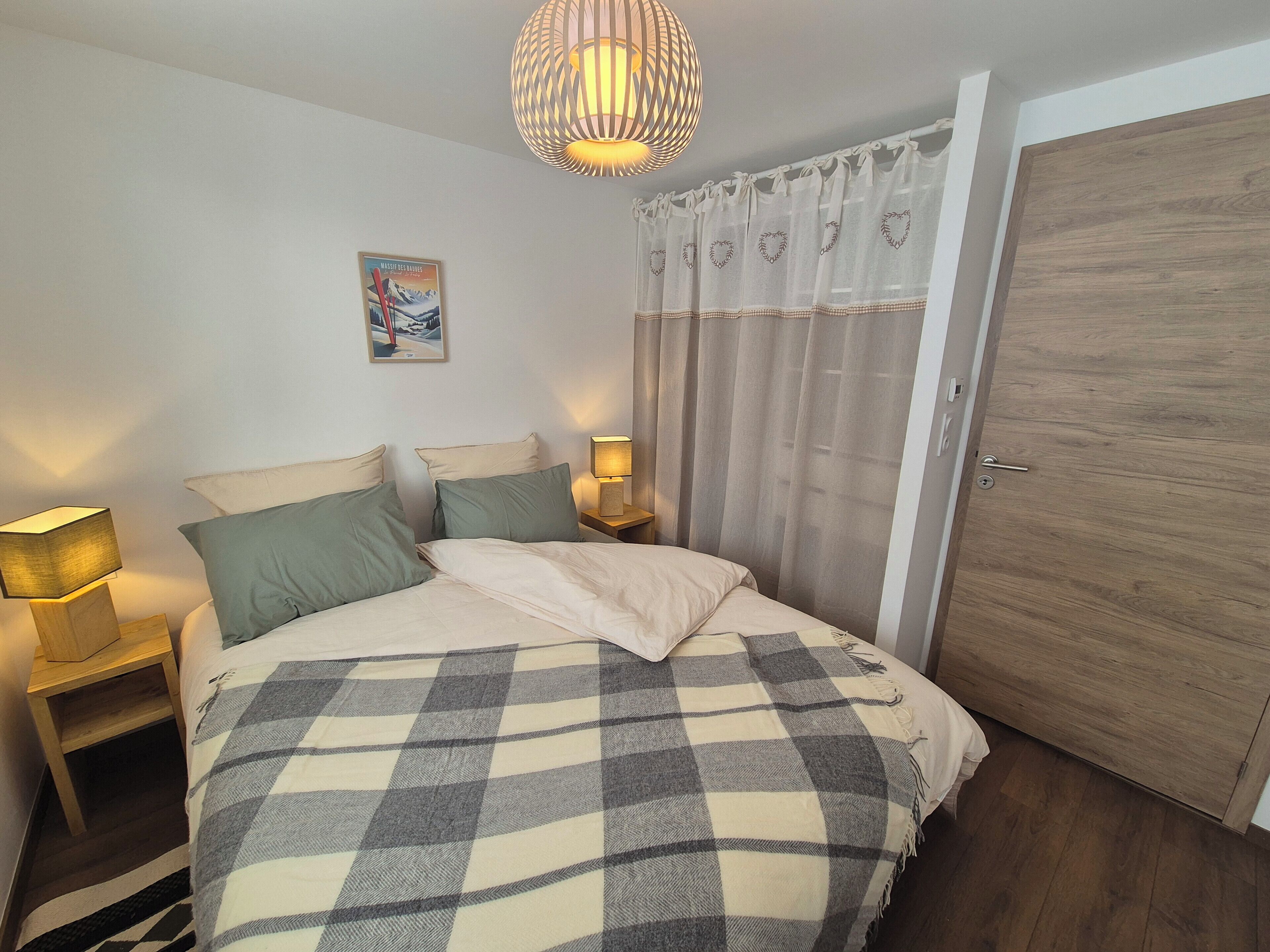 A bedroom with a bed, two bedside tables with lamps, a wooden door, and a painting on the wall.