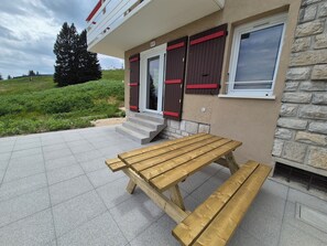 Ein Holztisch für ein Picknick vor einem Gebäude mit einer Steinmauer und einer Tür mit Fensterläden.