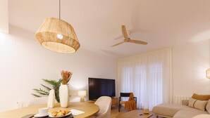 A modern living room with a round wooden table, beige sofas, a ceiling fan, and a TV. - Bravissimo Pou Rodó, 2 bedrooms and bike friendly (Girona)