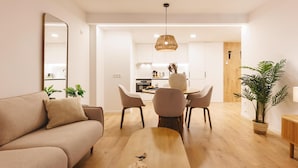 A modern living room with a sofa, a wooden coffee table, and a dining area with chairs and a hanging light fixture. - Bravissimo Pou Rodó, 2 bedrooms and bike friendly (Girona)
