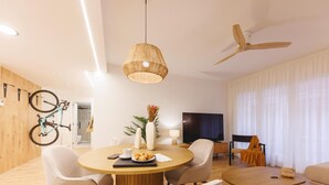 A modern living room with a round dining table, comfortable seating, a television, and a ceiling fan. - Bravissimo Pou Rodó, 2 bedrooms and bike friendly (Girona)