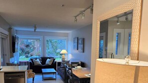 A modern kitchen with a wooden countertop, a dining area with a table and chairs, and a living room with a sofa and a TV. - Oceanside Gardens One Bedroom Ground Floor w/ Kitchen at Pacific Shores Resort! (Nanoose Bay)