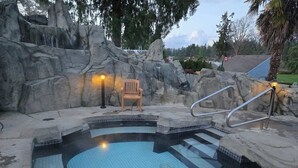 A hot tub with a tiled floor, surrounded by rock formations and a wooden chair. - Oceanside Gardens One Bedroom Ground Floor w/ Kitchen at Pacific Shores Resort! (Nanoose Bay)