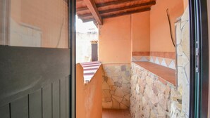 A narrow corridor with a stone wall and a tiled floor, leading to a small outdoor area.
