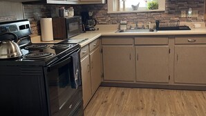 A kitchen with a stove, microwave, and sink. It has wooden cabinets and a stone backsplash.