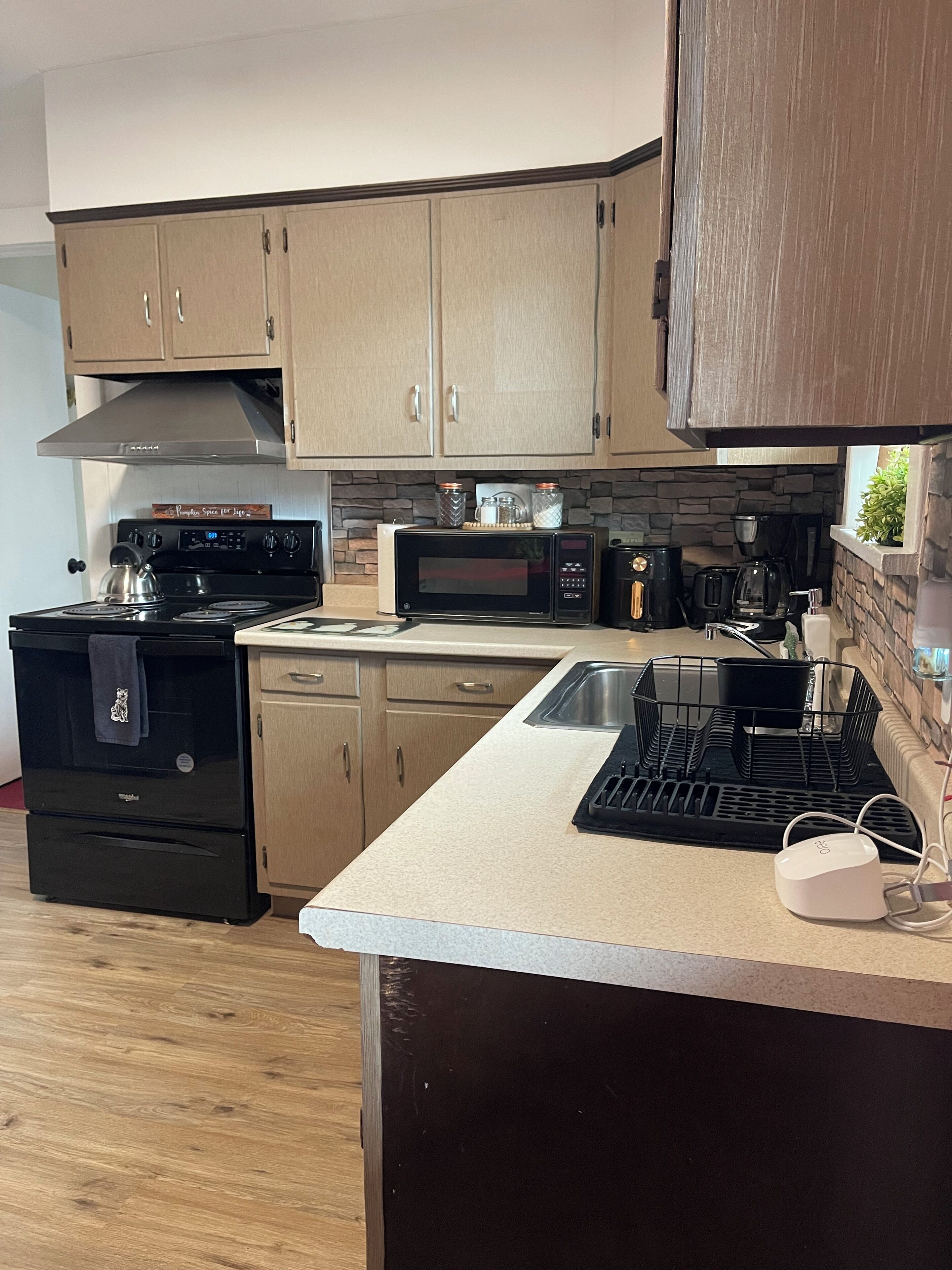 A modern kitchen with light wood cabinets, a stainless steel range hood, a microwave, a coffee maker, and a built-in oven.