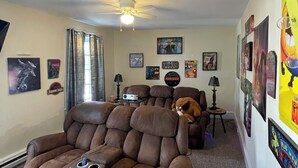 A living room with a reclining chair, a ceiling fan, and various posters on the walls.