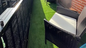 A balcony with artificial grass, wicker furniture, and a brick wall.