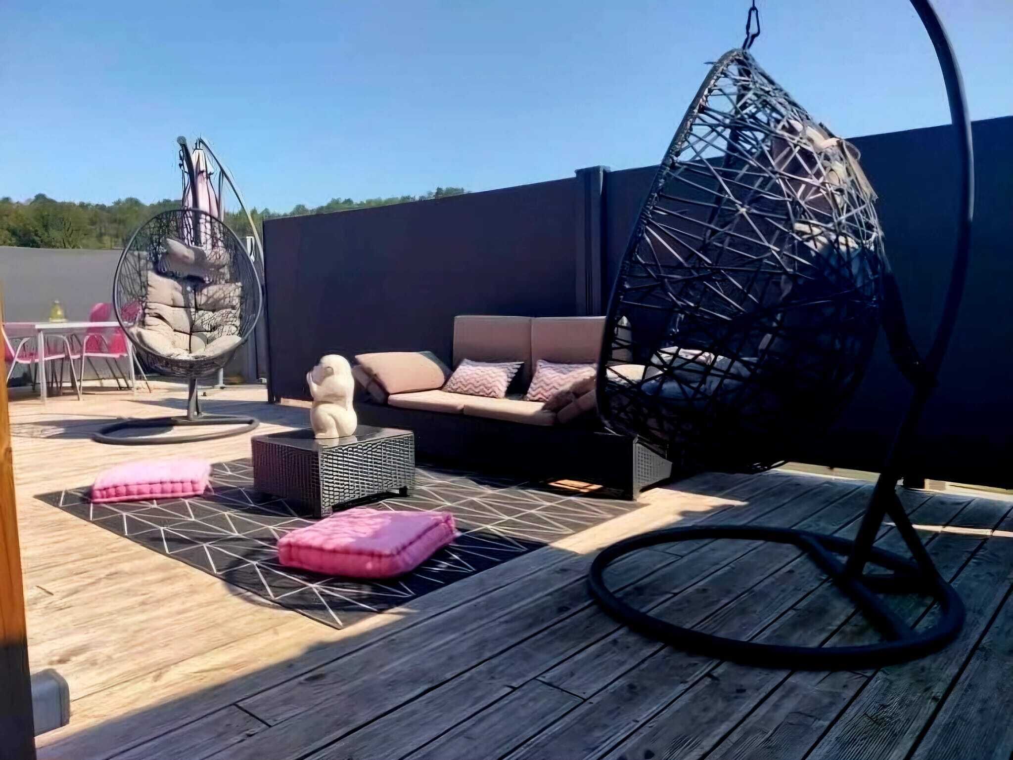 Una terraza de madera con una silla colgante, un sofá y una pequeña mesa con una estatua de perro.