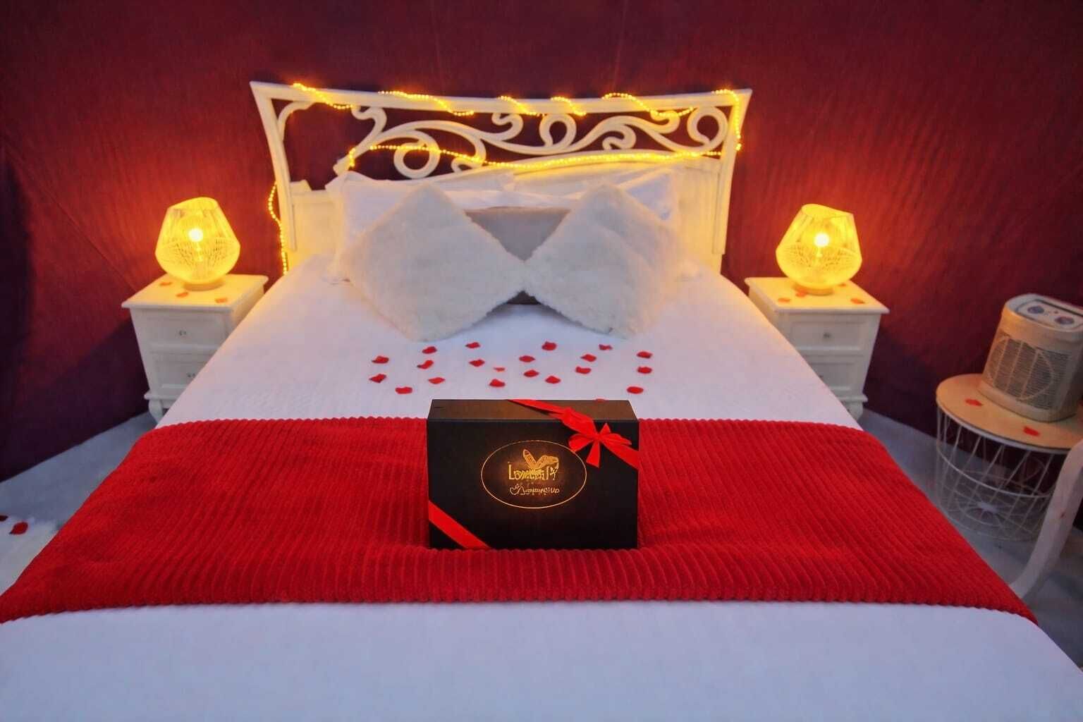 A bed with a red and white bedspread, a decorative pillow, and a gift box on the bed.